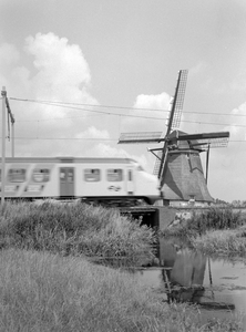 151021 Gezicht op een molen en een passerend electrisch treinstel mat. 1964 (plan V) van de N.S. ter hoogte van Hazerswoude.